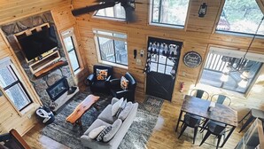 A cozy cabin interior with a fireplace, sofa, dining table, and large windows.