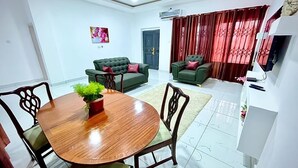 A living room with a wooden dining table, two green sofas, and a red curtain.