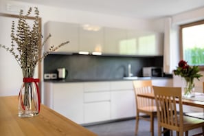 A modern kitchen with white cabinets, a wooden table, and a vase with dried flowers.