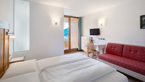Habitación de hotel con cama, sofá rojo, escritorio con silla, televisor y ventana con vistas.