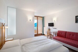 A hotel room with a bed, a red sofa, a desk with a chair, a TV, and a window with a view.