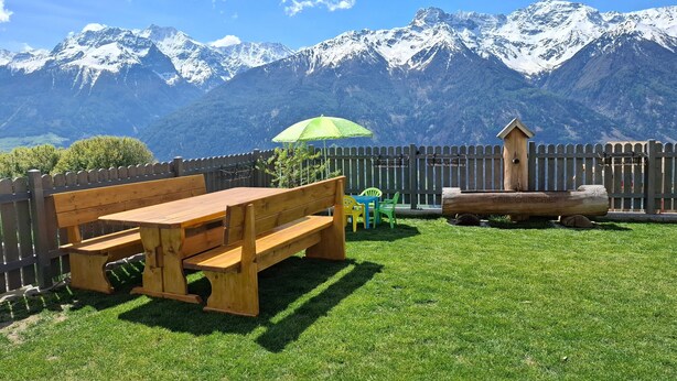 A wooden bench, a green umbrella, and a wooden birdhouse in a grassy yard with a mountain backdrop. - Apartment 'Morgenrot' with Mountain View, Shared Garden and Wi-Fi (Lasa)