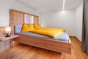Una cama de madera con colchón gris y almohadas amarillas en una habitación con suelo de madera y cabecera de madera.