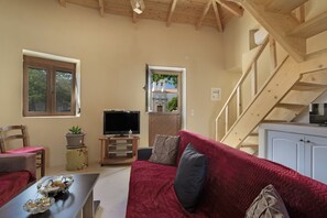 A living room with a red sofa, a television, a wooden staircase, and a view through a window. - Apartment 'Angel’s  1' with Shared Terrace, Wi-Fi and Air Conditioning (Kithira)