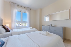 Een hotelkamer met twee bedden, een groot raam met gordijnen, een nachtkastje met lamp en een spiegel aan de muur.