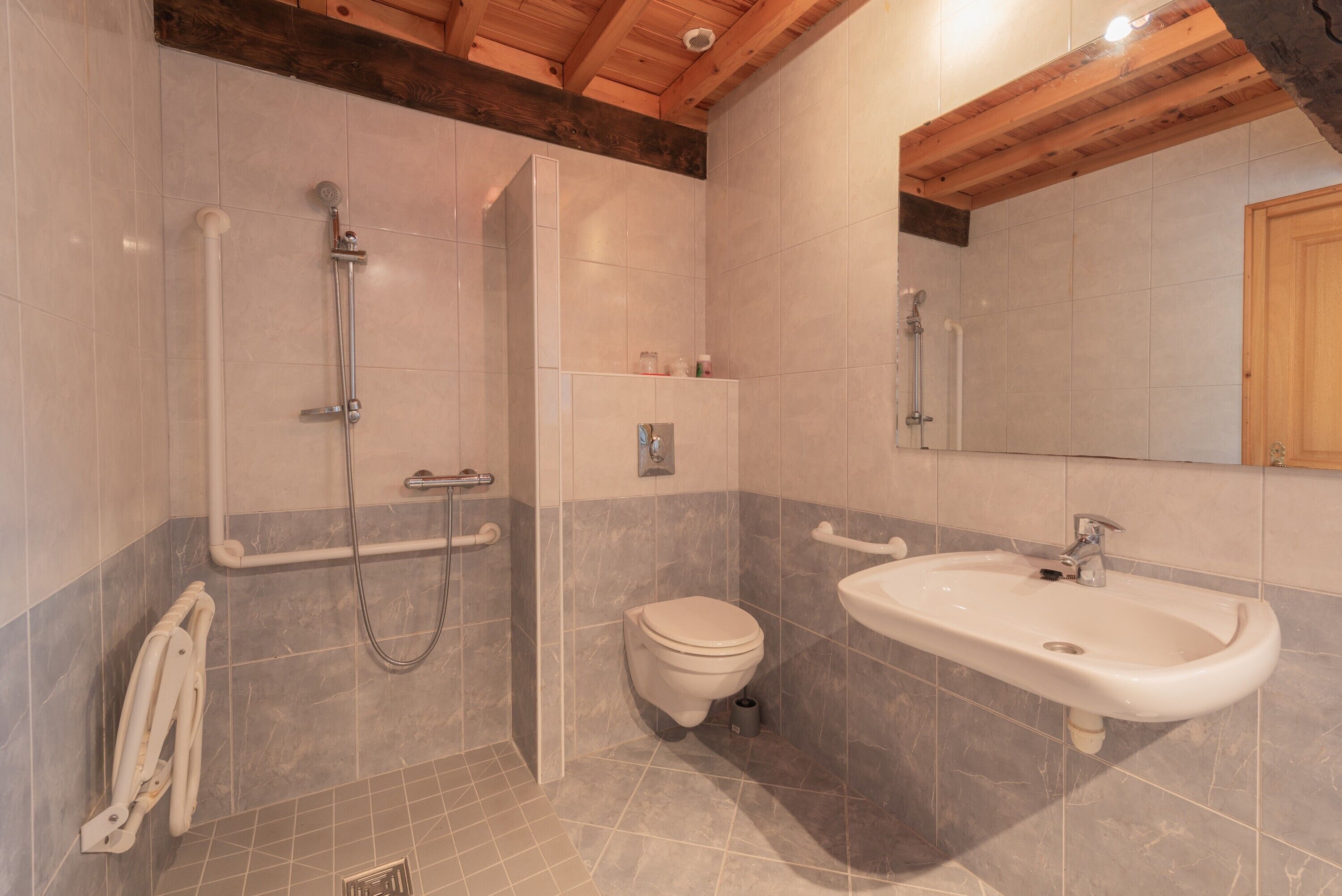 Ein Badezimmer mit Dusche, Toilette und Waschbecken, Holzbalkendecke und Fliesenwänden.