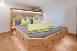 A wooden bed with a headboard, a grey mattress, and green bedding.