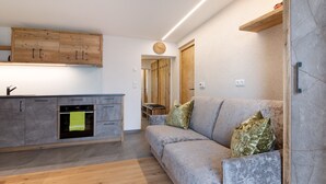 A modern kitchen with wooden cabinets, a built-in oven, and a grey sofa with cushions.
