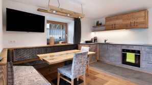 A modern kitchen with a wooden dining table, a built-in oven, and a TV mounted on the wall.