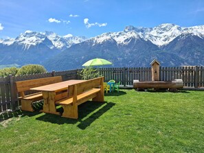 A wooden bench, a green umbrella, and a wooden birdhouse in a grassy yard with a mountain backdrop. - Apartment 'Heuduft' with Mountain View, Shared Garden and Wi-Fi (Lasa)
