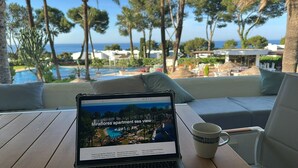 A laptop on a table with a view of a pool and palm trees. - Apartment 'Parque Miraflores' with Shared Pool, Wi-Fi and Air Conditioning (Mijas)