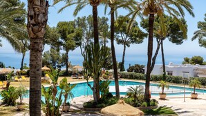 A pool area with palm trees, lounge chairs, and a view of the sea. - Apartment 'Parque Miraflores' with Shared Pool, Wi-Fi and Air Conditioning (Mijas)