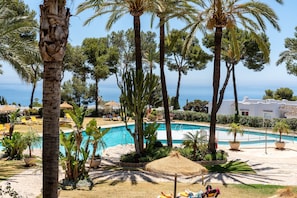 Zona de piscina con palmeras, sillones de descanso y vista al mar.