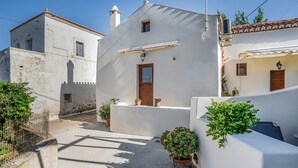 Une rue étroite bordée de bâtiments blancs, avec une porte en bois et des plantes en pot.