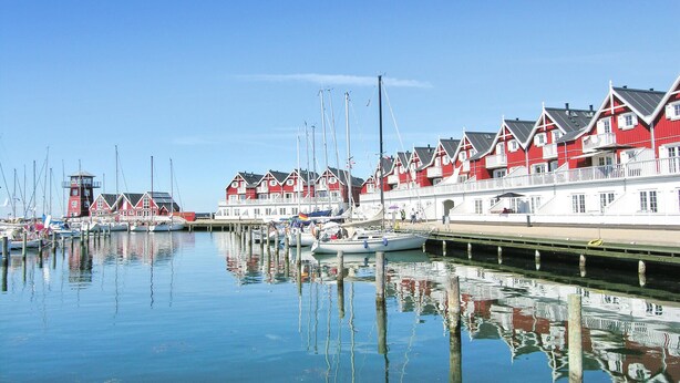 Een jachthaven met rode en witte gebouwen, boten afgemeerd en rustig water.