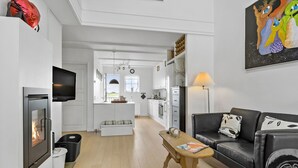 Een moderne woonkamer met een open haard, een bank, een bijzettafeltje en een keuken op de achtergrond.
