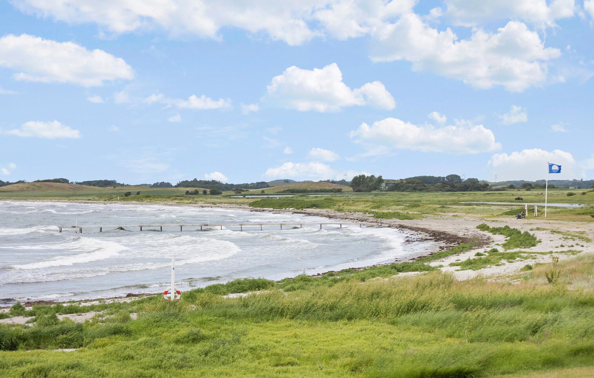 Un paysage côtier avec une plage de sable, des dunes herbeuses et un ciel dégagé.