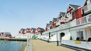 Een pand aan het water met rode en witte gebouwen, een steiger en een grindpad.