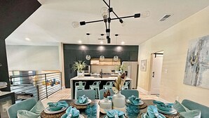 Een moderne eethoek met een centraal eiland, teal stoelen en een zwarte tafel.