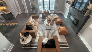 Een moderne woonkamer met een zithoek, een salontafel en een televisie. Twee deuren leiden naar andere kamers, en een raam met gordijnen.