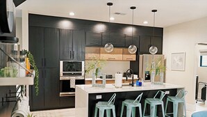 Een moderne keuken met donkere kastjes, een centraal eiland met barstoelen, hanglampen en een magnetron.