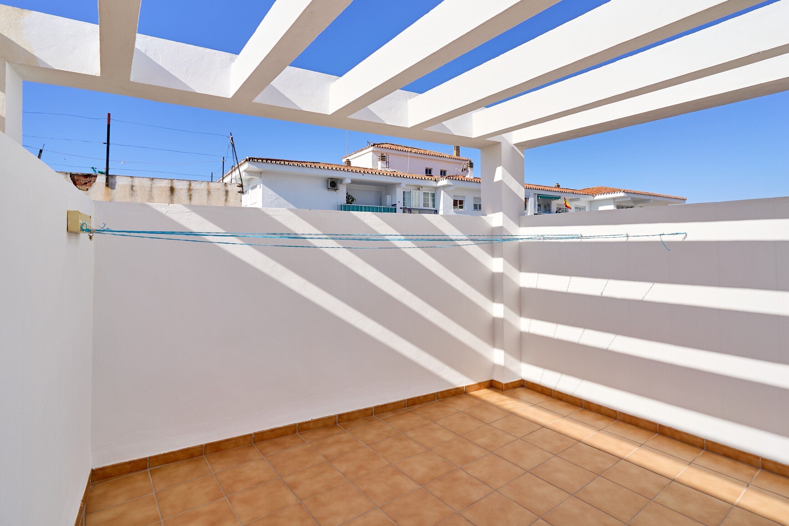 Un balcone con ringhiere bianche e pavimento piastrellato, con vista su un edificio con tetto in tegole.