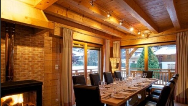 Un interior de madera con chimenea, una mesa de comedor lista para seis comensales y ventanas amplias.
