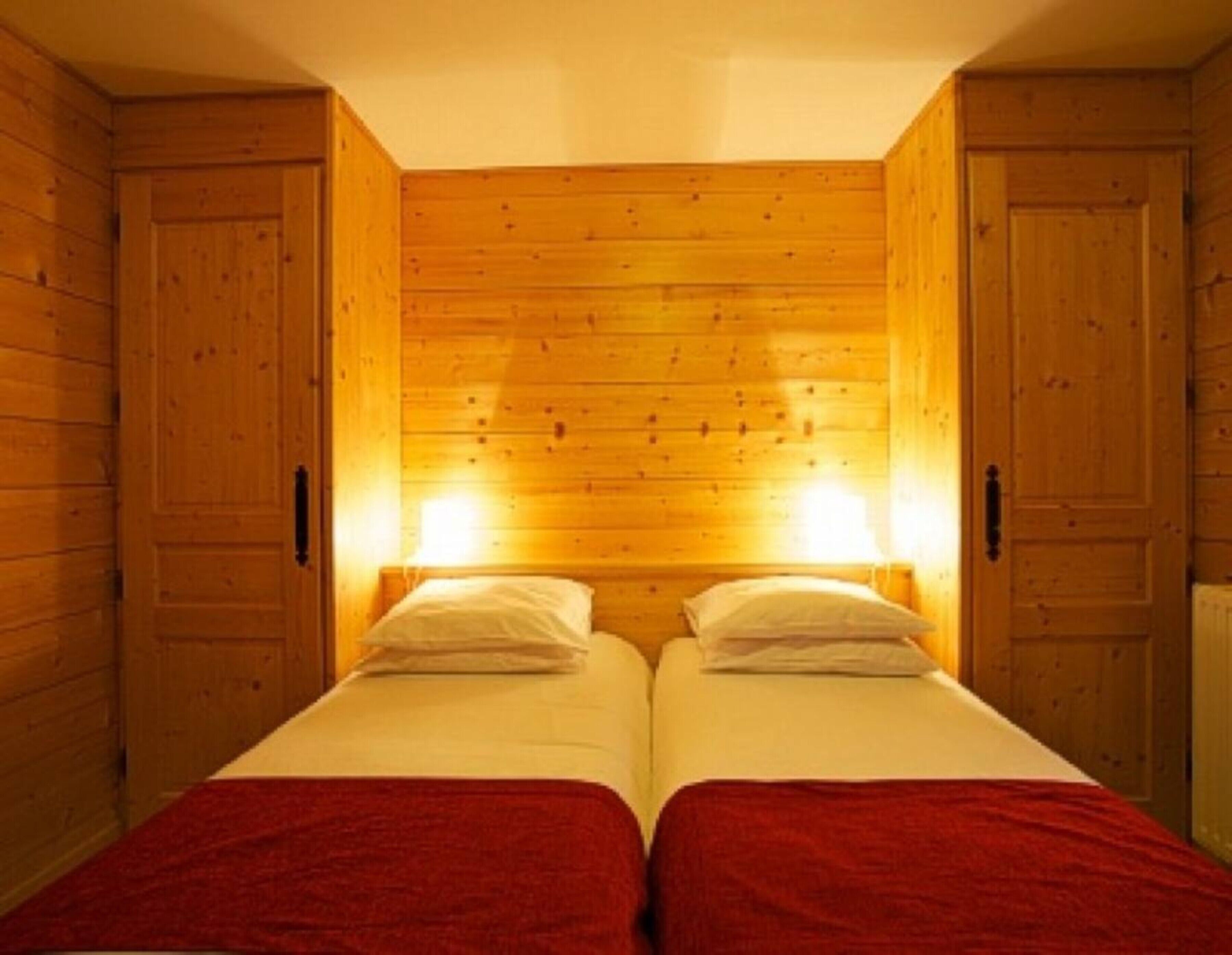 A room with two beds, wooden walls, and two wall-mounted lights.