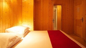 Una habitación de madera con una cama, una alfombra roja y una puerta.
