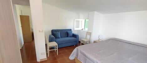 A bedroom with a bed, a blue sofa, a small table, and a chair.
