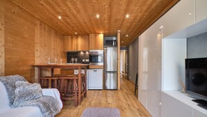 A cozy cabin interior with a wooden ceiling, a kitchen area with modern appliances, a dining table, and a comfortable seating area.