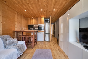 L’intérieur chaleureux d’un chalet avec un plafond en bois, un coin cuisine équipé d’appareils modernes, une table à manger et un coin salon confortable.