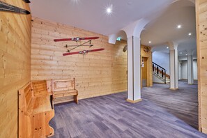 Un intérieur en bois, avec des paires de skis accrochées au mur, un banc et un escalier en arrière-plan.