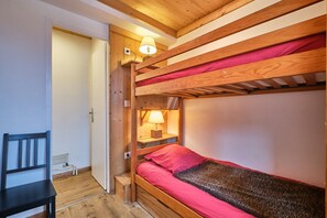A bunk bed with a red mattress, a wooden chair, and a lamp on a bedside table.