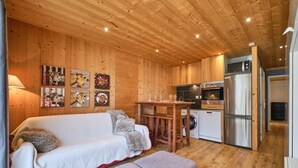 A wooden interior with a sofa, ottoman, kitchen area, and wall art.
