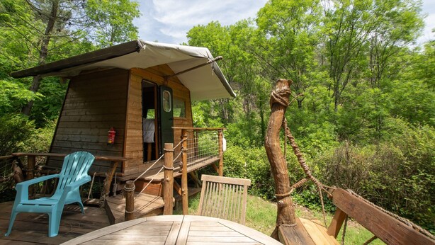 A wooden cabin with a covered deck, a rope bridge, and a blue chair. - Caravan 'La Pêcherie' with Private Terrace (malbosc)