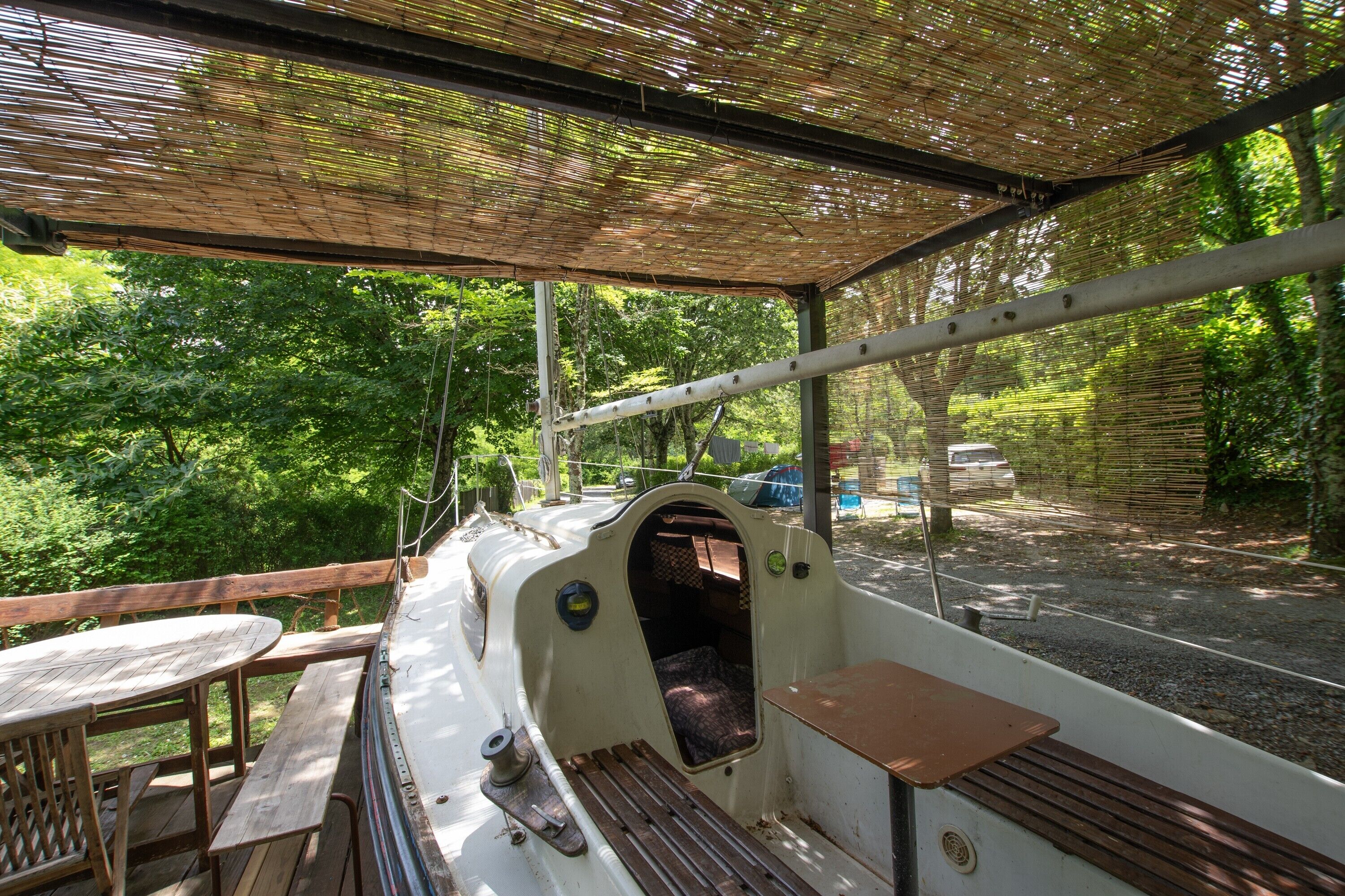 Un espace extérieur abrité, avec une table et des bancs, entouré de verdure.