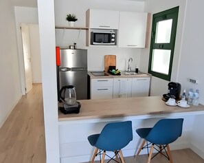 Eine kleine Küche mit Mikrowelle, Kühlschrank, Spüle und Barhocker.