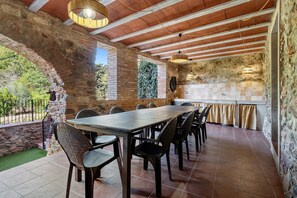 Un espacio comedor al aire libre con techo, una pared de piedra, una mesa de madera y sillas.