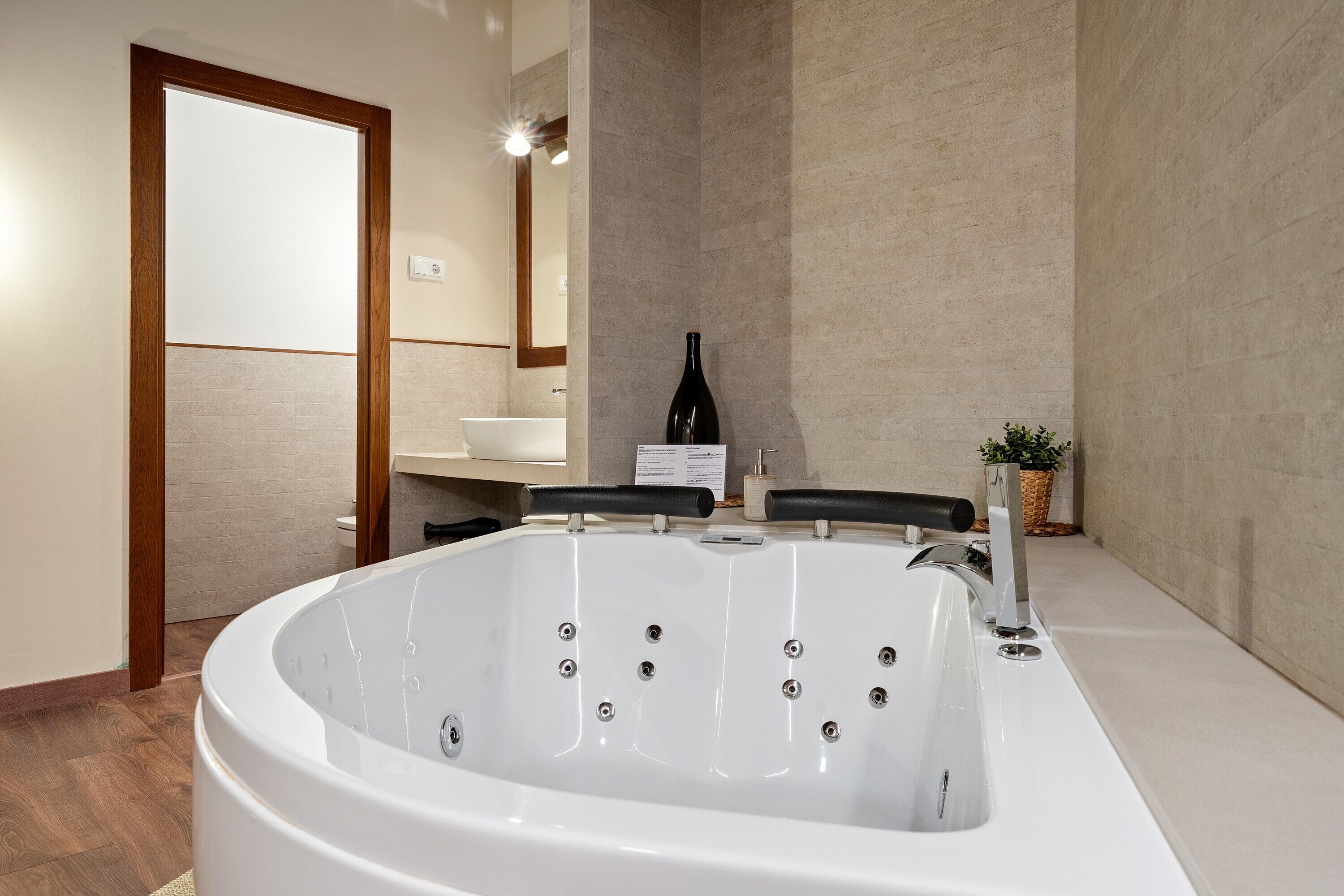 A modern bathroom with a large bathtub, a wooden door, a white sink, and a mirror.