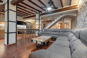 Una sala de estar moderna con un sofá modular, una mesa de centro de madera con ruedas, una zona de cocina y una escalera.