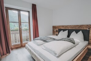 Ein Schlafzimmer mit einem Holzkopfteil, einem großen Bett mit weißer Bettwäsche und Blick durch eine Schiebetür.