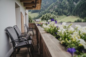 Un balcon avec des chaises et une balustrade en bois, donnant sur un paysage montagneux.