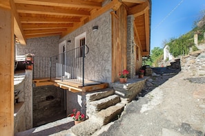 A stone building with wooden beams, a balcony with a metal railing, and potted plants.