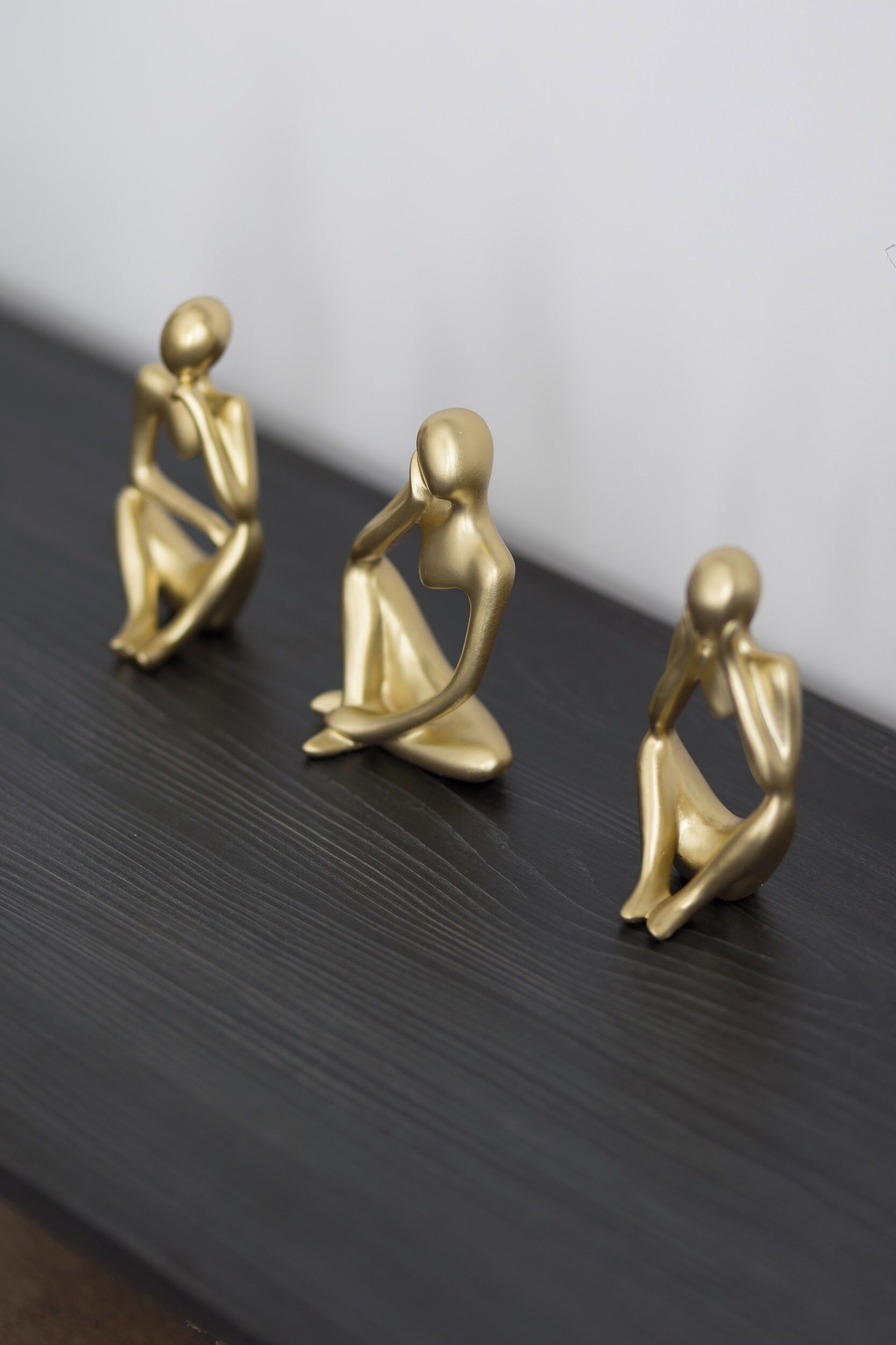 Drei goldene Statuen auf einer dunklen Holzfläche.