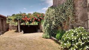 A courtyard with a stone wall, a small building, and flowering plants. - Country House 'María Bargiela' with Private Terrace, Private Garden and Wi-Fi (A Picaraña)