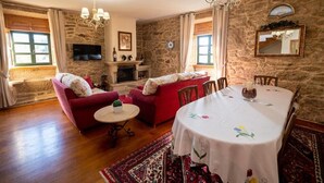 A living room with a fireplace, stone walls, a dining table with a white tablecloth, and red sofas. - Country House 'María Bargiela' with Private Terrace, Private Garden and Wi-Fi (A Picaraña)