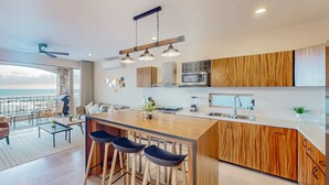 Una cocina moderna con una isla de madera, taburetes de bar y vistas al océano.