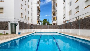 Une piscine à l’eau d’un bleu limpide, entourée de bâtiments blancs dotés de balcons et d’un portail.