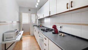 Une cuisine avec des meubles blancs, un four à micro-ondes, un batteur rouge et une cuisinière à gaz.